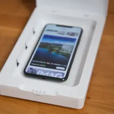 Czy odkażanie telefonu promieniami UV to skuteczna metoda na bakterie? Smartfon w białym pudełku z lampami UV, gotowy do dezynfekcji.