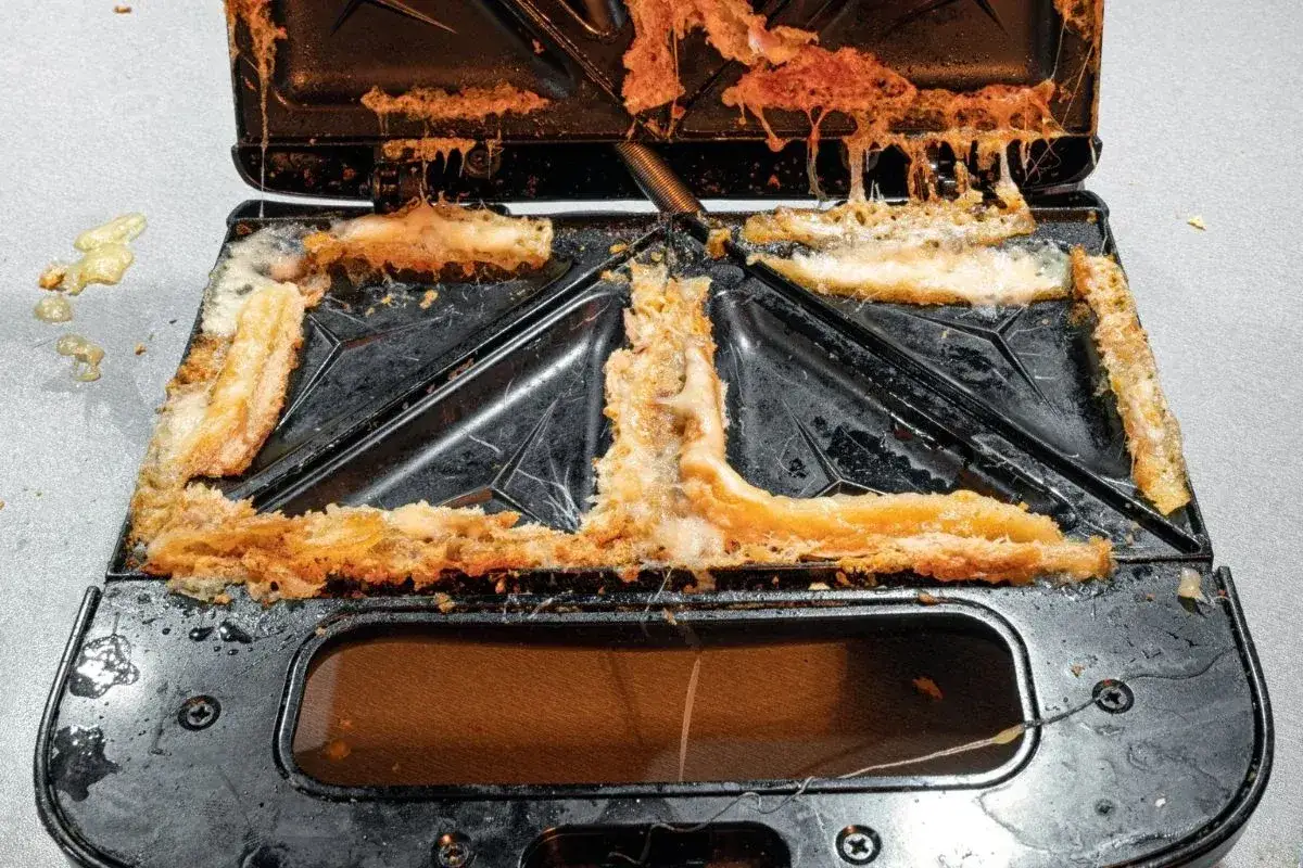 Jak wyczyścić przypalony toster sandwich bez zalewania elektroniki wodą? Widok mocno zabrudzonego wnętrza opiekacza z resztkami sera i przypalonego pieczywa.