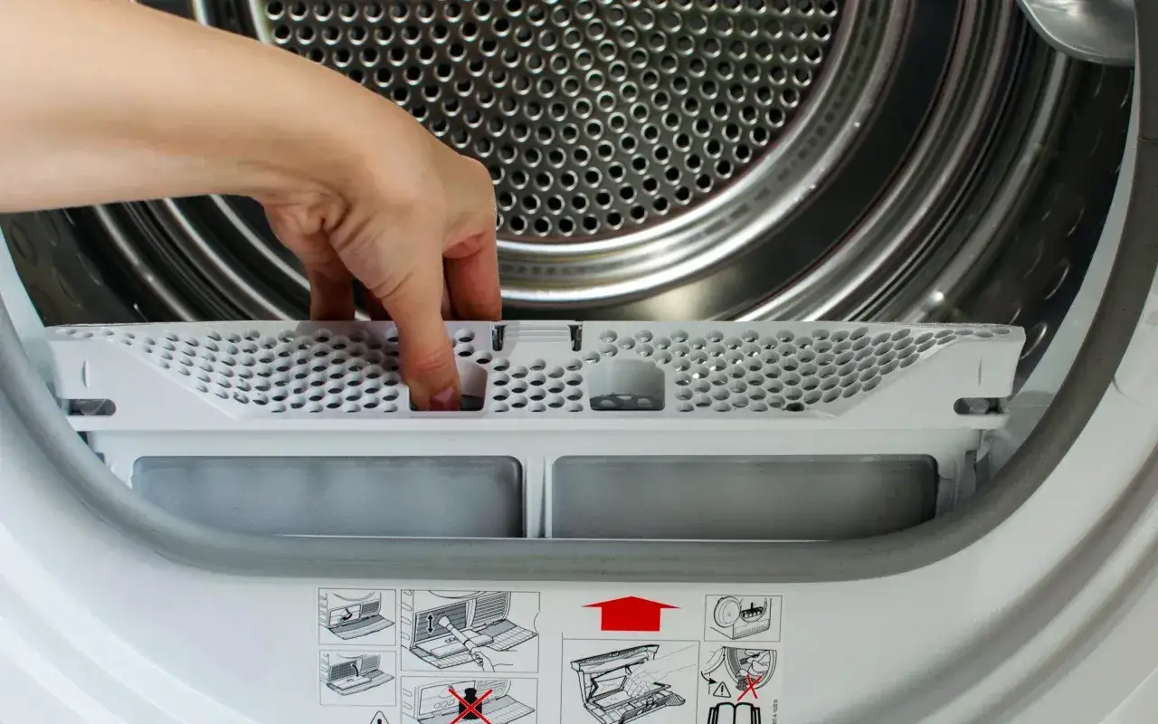 Dłoń wyjmuje filtr z suszarki bębnowej. Czyszczenie filtra to klucz do tego, jak wyczyścić filtr w suszarce bębnowej żeby ubrania szybciej schły.