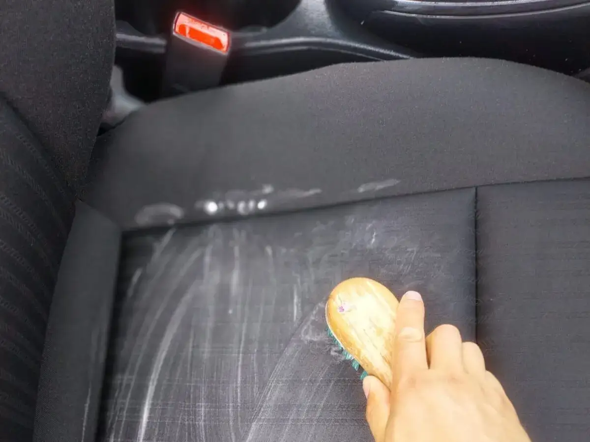 Domowy sposób na plamy z kawy na jasnej tapicerce samochodowej. Ręka szczotkuje siedzenie, usuwając ślady po kawie.